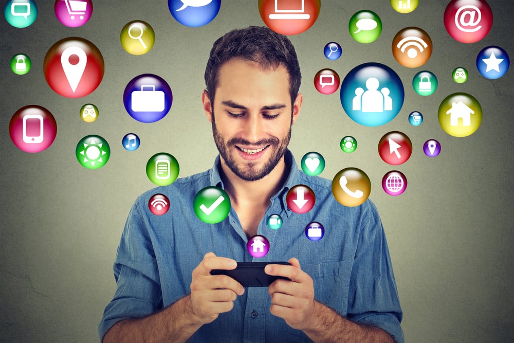 communication technology mobile phone high tech concept. Happy man using texting on smartphone social media application icons flying out of cellphone isolated grey wall background. 4g data plan communication technology mobile phone high tech concept. Happy man using texting on smartphone social media application icons flying out of cellphone isolated grey wall background. 4g data plan